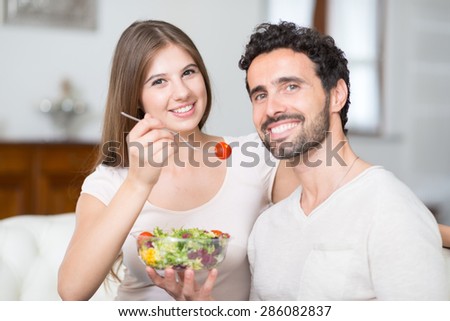 Couple eating a salad in the living room. Shallow depth of field, focus on the woman