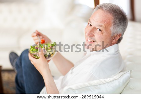 Mature man eating a healthy salad sitting on his couch