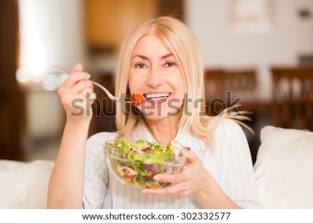 Portrait of a smiling woman eating an healthy salad in her living room