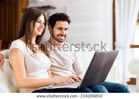 Portrait of an happy couple using a laptop computer in their house. Shallow depth of field, focus on the woman