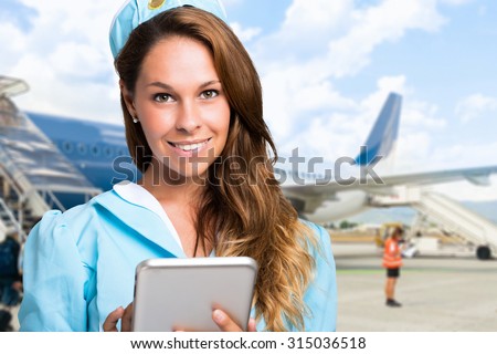 Portrait of a smiling stewardess using a tablet in front of an airplane