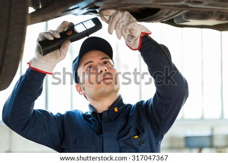 Mechanic using a light to inspect a lifted car