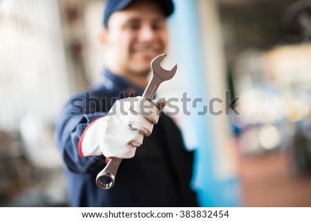 Smiling mechanic holding a wrench in his shop