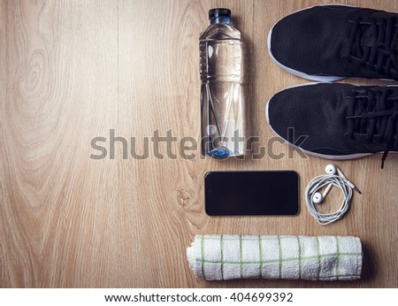 Sport equipment, Sneakers, water, towel, phone and earphones on wooden background, Flat lay