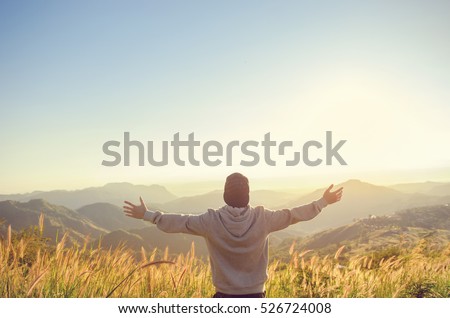 Carefree Happy Man Enjoying Nature on grass meadow on top of mountain cliff with sunrise. Beauty Outdoor. Freedom concept. Sunbeams. Enjoyment. copy space.