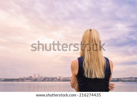 blonde girl looks at the evening city near the river.