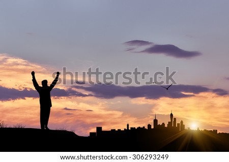 Silhouette of a happy man with his arms on the background of evening city cloudy sky with sun rays