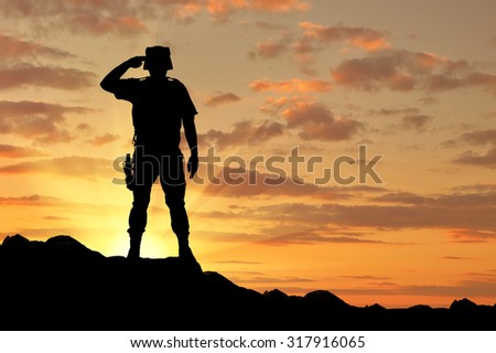 Silhouette of a soldier salutes at sunset
