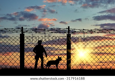 Silhouette of a soldier on the border with a fence and a dog at sunset