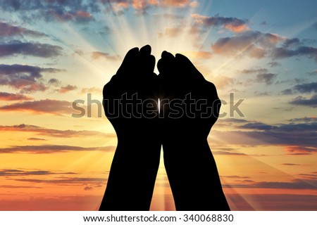 Concept of Islam, the Koran. Silhouette of praying hands facing the sky at sunset