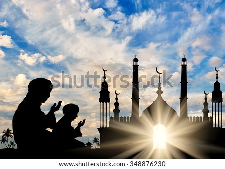 Concept of the Islamic religion. Silhouette of two men praying on the background of the town hall at dawn