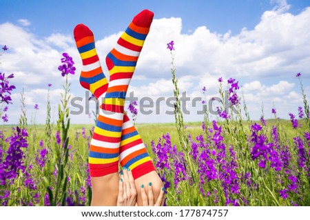 Funny woman leg in flower field and cloudy sky. Summer vacation concept