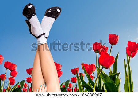 Sexy woman legs in summer sandals over blue sky and flower field background. Summer vacation concept