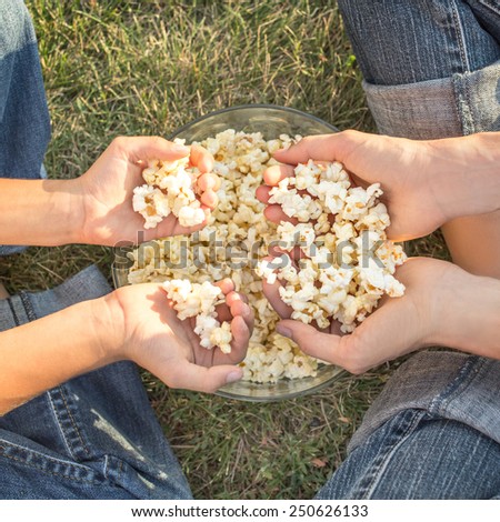 Family eat popcorn sitting on grass, focus on hands with popcorn