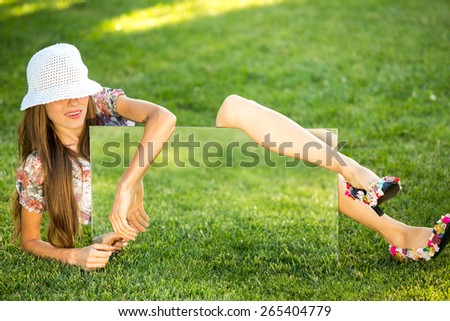 Beautiful young woman wearing hat over green grass natural background laying and holding mirror with green grass reflection