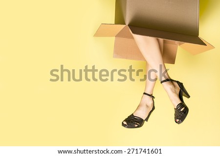 Funny shopping concept, woman legs sticking out from box over bright yellow background. copy space, soft studio shot