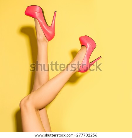 Female legs wearing summer high heels over yellow background