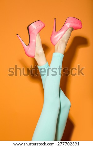 High fashion look. Sexy female legs wearing high heels and mint pants over orange background