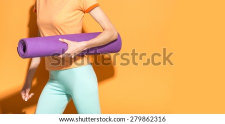 Closeup detail woman holding yoga mat over bright orange background, copy space. Yoga girl concept