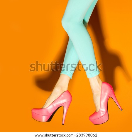 Female legs wearing high heels over orange background