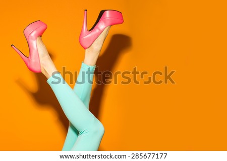 Female legs wearing high heels over bright orange background