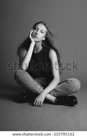 Young beauty blond woman seating, touching her face, black and white, grey background.