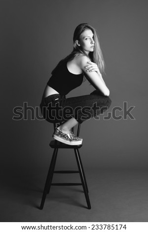 Beauty young blond girl seating on the high chair, grey background.