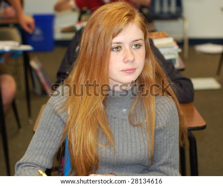 Strawberry blonde teenager taking notes in a classroom