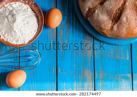 Baking cake in rural kitchen - dough recipe ingredients eggs, flour, butter, bread and whisk on vintage wood table from above. Rustic background with free text space.