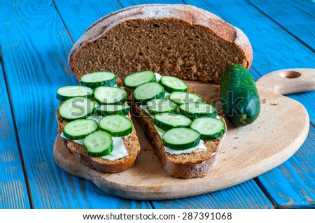 Freshly baked bread, cucumber and sandwich with sliced cucumbers in rural or rustic kitchen on vintage wood table from above. Background