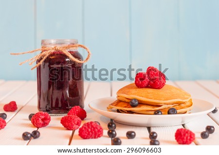 Stack of wheat golden pancakes or pancake cake with freshly picked raspberry on a dessert plate, glass mason jar full off blueberry jam