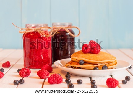 Stack of wheat golden pancakes or pancake cake with freshly picked raspberries on a dessert plate, glass mason jar full off blueberry and raspberry jam