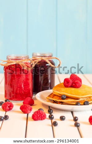 Stack of wheat golden pancakes or pancake cake with freshly picked raspberries on a dessert plate, glass mason jar full off blueberry and raspberry jam