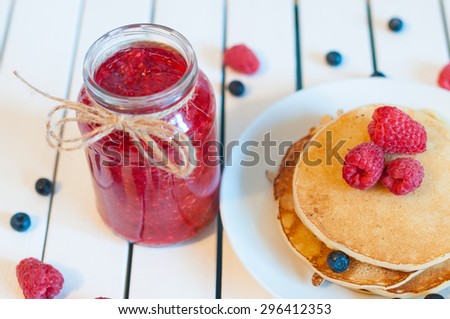 Stack of wheat golden pancakes or pancake cake with freshly picked raspberry on a dessert plate and raspberries marmalade at jam jar. Top view.