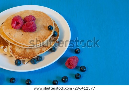 Stack of wheat golden pancakes or pancake cake with freshly picked raspberry on a dessert plate. Top view, with empty space for text