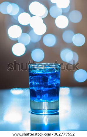 an alcoholic blue cocktail is in glass, on the bar wiyh magic bokeh light.