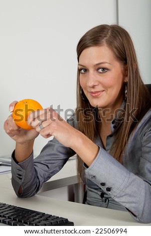 young beautiful woman eating an orange in her office