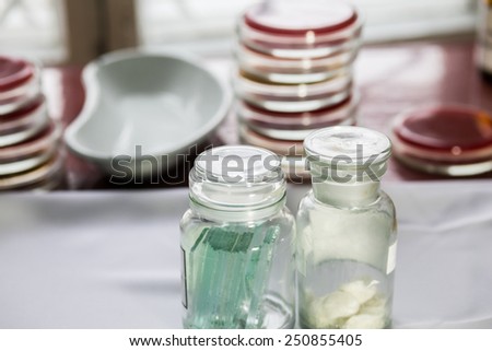 Bottles with glass pieces and swabs in a lab; Petri dishes stacked on the background. Medical tests and research. Hospital labotory glassware.