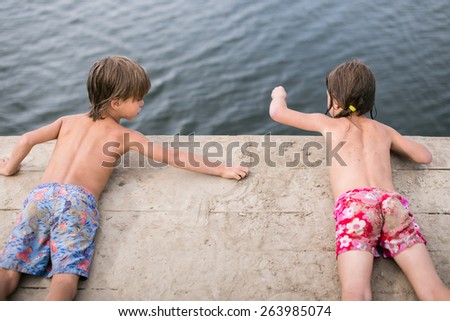 Fraternal twins tanning and playing with sand on wooden deck at the lake on hot summer day. Family having fun during vacation.