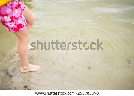 Toddler feet in water at the beach. Child in pink shorts walking barefoot in transparent lake water. Having fun at summertime.