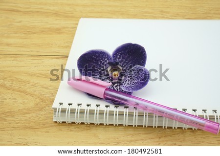 Empty notebook no text. The edge is spiral binder, has one pink pen and one purple flower on the notebook.