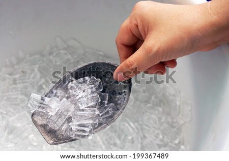 Hand is holding the ice scoop, in a cooler packed with ice.