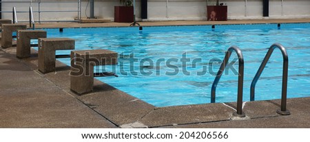 Public pool with clear blue water, stand for jump and see a ladder for access to the swimming pool.