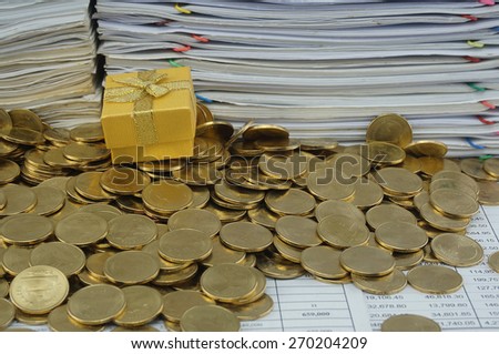 Gold gift box in heap of gold coins with pile of paperwork.