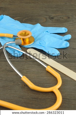 Medical examination such as stethoscope, wooden tongue depressor and glove placed on table.