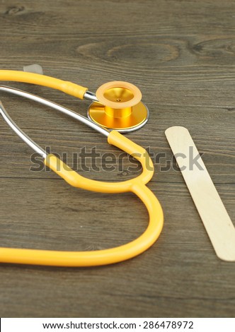 Wooden tongue depressor and stethoscope placed on table in examination room.