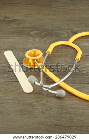 Wooden tongue depressor and stethoscope placed on table in examination room.