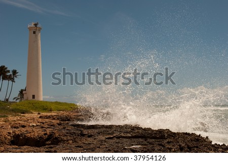 Wave crashing into rocky shore, Barber's Point Lighthouse in background, taken on Oahu, Hawaii.