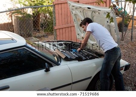 Car Trouble. Man working on car in back yard. Do it yourself mechanic performing auto repair. Examining engine compartment; diagnose and fix / correct problem; preventative maintenance.