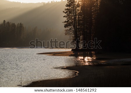 Diffused sunlight hits mountain light as sun sets through the trees at a mountain lake.